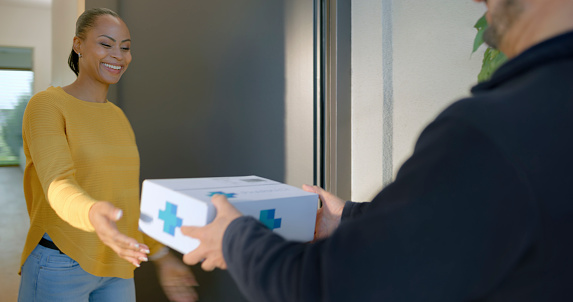 Medicine delivery person delivering medicine to smiling woman at home.