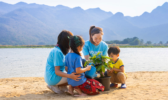 Team of volunteer worker group teaching children to planting tree in charitable social work on forest rewilding NGO work for fighting climate change and global warming in the coastline habitat