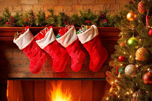 Photo of Christmas stockings hanging from a mantelpiece above glowing fireplace