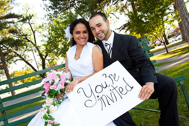 Bride and Groom outside with sign reading You're Invited
