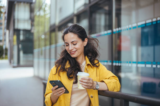Woman texting and drinking coffee outdoors. Shot of a beautiful mature businesswoman texting. Mature businesswoman walking outdoors and using cellphone. Female business professional walking outside and texting from her mobile phone. liverpool one stock pictures, royalty-free photos & images