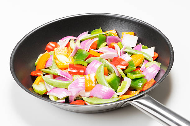 Colorful and fresh vegetables in a non-stick frying pan on a white background (red, green and orange bell peppers, onions, green beans and celery). More vegetables...