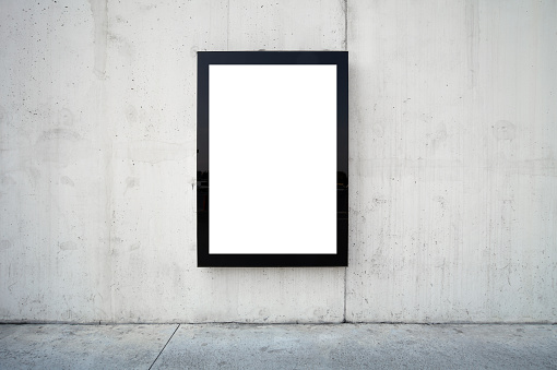 Blank billboard on wall. Wall is made of concrete and gray coloured. Billboard is oriented vertically and standing on the middle of frame. Edges of billboard are black. Billboard is empty so you can write or add something on it. - Clipping path of billboards included.