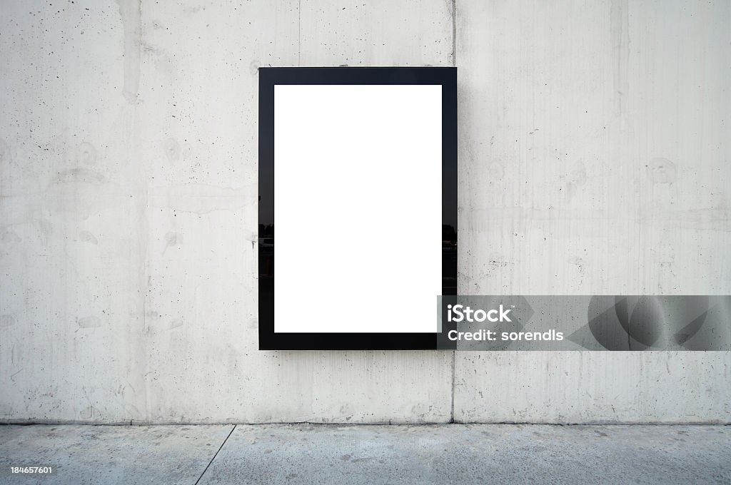 Blank billboard on wall. Blank billboard on wall. Wall is made of concrete and gray coloured. Billboard is oriented vertically and standing on the middle of frame. Edges of billboard are black. Billboard is empty so you can write or add something on it. - Clipping path of billboards included. Billboard Stock Photo