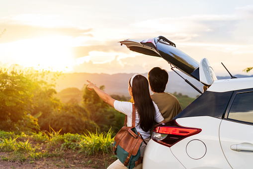 Young couple traveler with car watching a beautiful sunrise over the mountain while traveling road trip on vacation, Travel concept