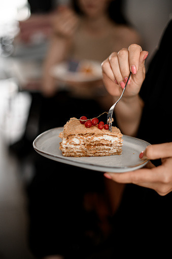 Selective focus on woman tasting classic french dessert millefeuille decorated with red currant, cropped shot. Delicious french pastry in bakery or cafeteria