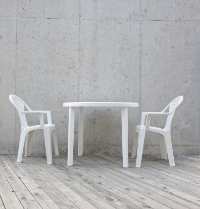 White plastic garden furniture on wood deck against concrete wall.