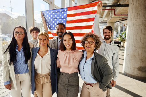 Large group of happy entrepreneurs with American flag standing in a hallway of an office building and looking at camera.