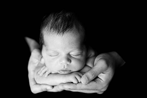 Black and White Image of Newborn Sleeping in Father's Hands
