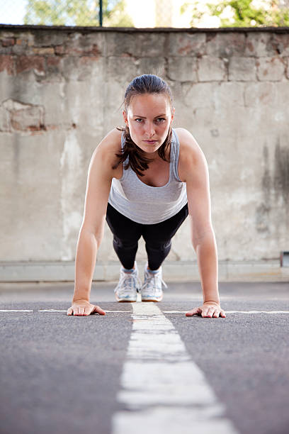 Young woman doing Burpee exercise "Young woman with intense look, in step three the pushup postion of  Burpee exercise. Vertical shot." burpee stock pictures, royalty-free photos & images