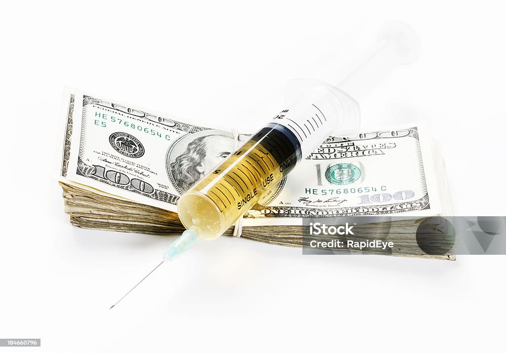 Injection of cash: expensive medication or profitable drug dealing Disposable syringe containing amber fluid rests on a fat bundle of US dollars. Could relate to the high cost of medication or the big profits from drug dealing. Isolated on white. American One Hundred Dollar Bill Stock Photo