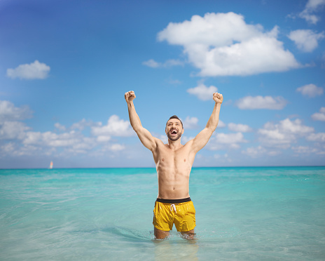 Excited man in a swimming suit standing in the sea and raising arms