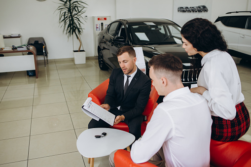 This is good choice. Confident young salesman explaining all the car features to the young attractive owners.