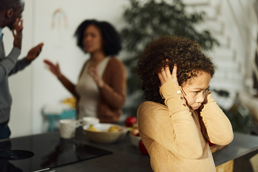 African American little girl refusing to her while her parents are arguing in the background.