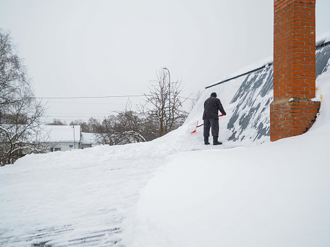 A man clears the roof of snow with a shovel during a snowfall.
