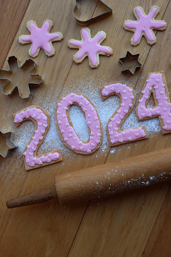 Shortcrust cookies with pink heart sprinkles in the form of numbers 2024, rolling pin and metallic cookie cutters on wooden table
