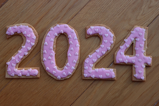 Shortcrust cookies with pink heart sprinkles in the form of numbers 2024  on wooden table