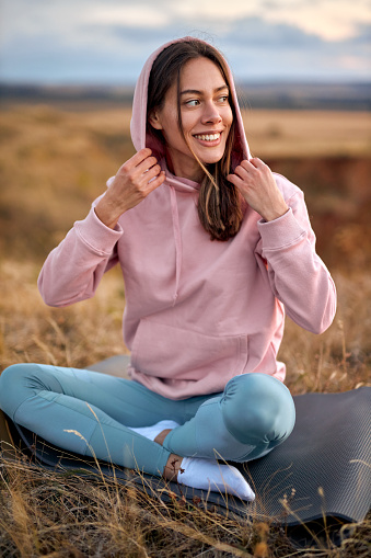 Happy smiling Adult woman relaxing on mat during yoga exercise, morning routine, sunrise light, outdoor. young female in sportswear stretching at nature open air. sport, healthy lifestyle.