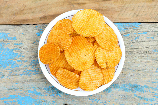 Potato chips in a plate on wooden background top view