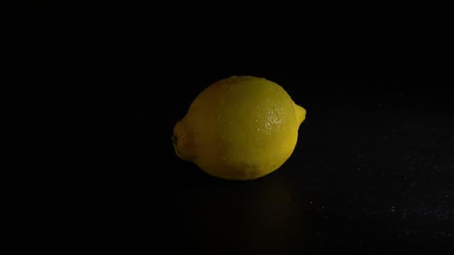 Vibrant Yellow Lemon Covered in Glistening Water Droplets Emerges from Darkness on a Black Background