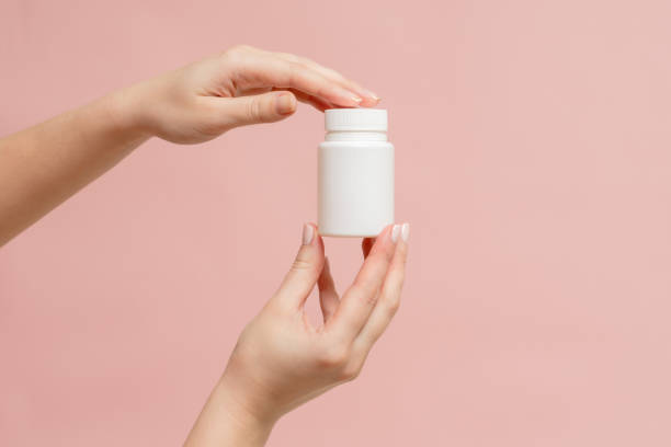 istock White bottle (plastic tube) in hands on pink background. Packaging for vitamins, pill or capsule, or supplement. Mockup for product branding 1846678915
