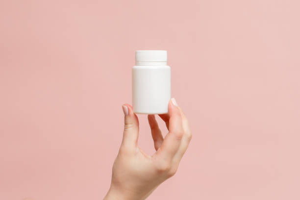 istock White bottle (plastic tube) in hand on pink background. Packaging for vitamins, pill or capsule, or supplement. Mockup for product branding 1846678917