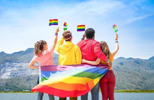 group of diverse lgbtq friends wearing colorful clothes, standing side by side, smiling and holding lgbt flags waving in the air, concept of lgbt community equality movement, lgbt happy pride month