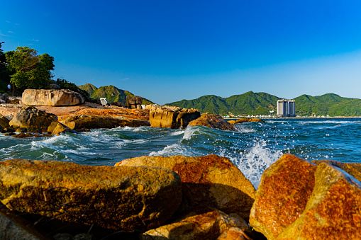 A sea wave is beating against the rocks near the seashore. Filmed at sunset near the rock garden in Nha Trang, Vietnam.