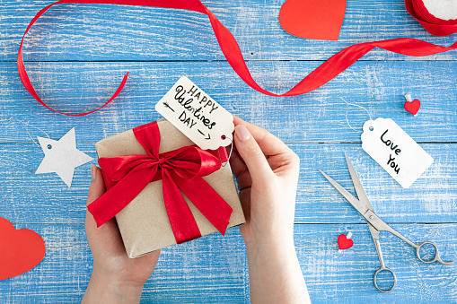 Valentine's Day background with gift box with red bow and decorative details on blue wooden background, top view.