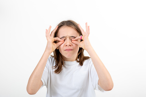 Funny teenage girl in a white T-shirt touches her eyes on a white background isolated.