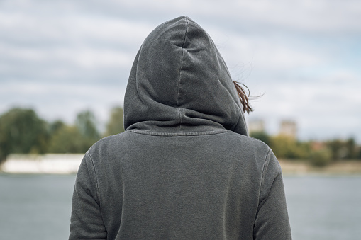 Rear view of woman wearing grey hoodie standing on the river bank in cold autumn morning