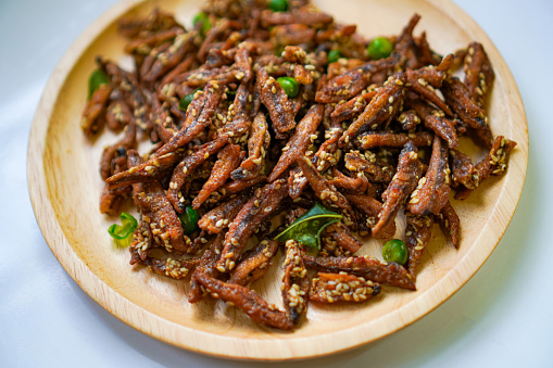 Side view of ready-to-eat Crispy Anchovy with Herb snacks on a wooden food plate.