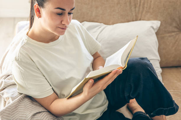istock Young woman reading a book at home, relaxing on the sofa. 1846764890