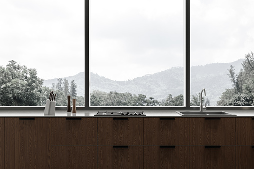 Dark home kitchen interior with wooden shelves, kitchenware and stove with sink. Cozy minimalist cooking space in modern apartment with panoramic window on countryside. 3D rendering