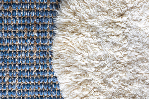 Hand woven geometric denim area rug and white carpet with long pile, home background texture.