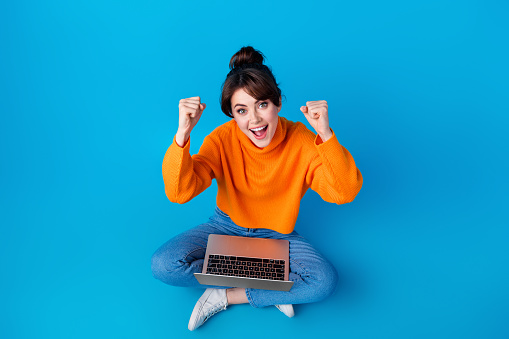 Full length top view photo of positive lucky lady wear knitted pullover rising fists winning game modern device isolated blue color background.