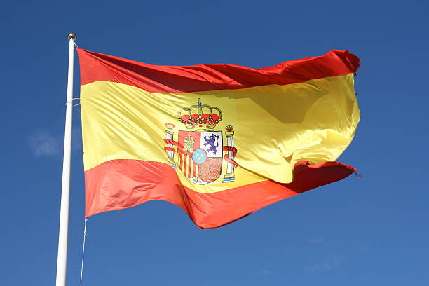 flag of spain waving in breeze with blue sky behind - spanje stockfoto's en -beelden