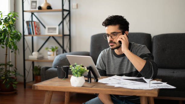 istock Young handsome man talking on the phone while working with tablet at home 1846808274