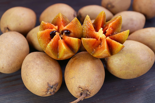 Beautifully Cut Sapodilla Fruit and Heap of Whole Fruits on Black Wooden Background