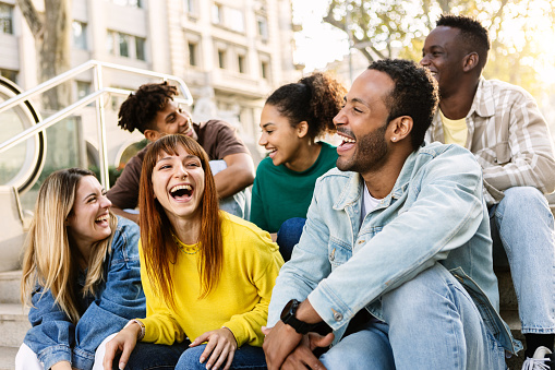 Young group of hispanic latin friends having fun together outdoors. Millennial multiracial people laughing while social gathering sitting on stairs at city street
