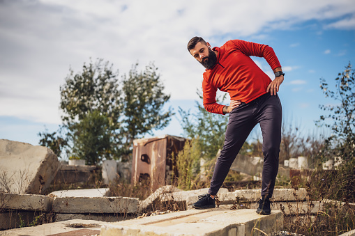 Adult man is exercising outdoor on sunny day. He is stretching his body.