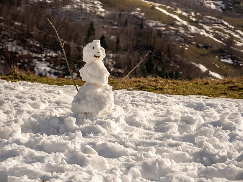 A snowman standing atop a snowy incline, illuminated by the bright winter sun