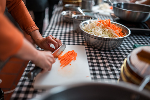 Close-up of multiracial group experience and learn the art of Chinese cuisine as they skillfully prepare ingredients for a flavorful vegetable stir-fry delight on a cooking class with beautiful Chinese female chefs.