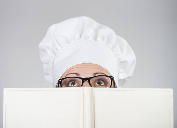 istock Woman in chef's hat looking over the cookbook 184689825