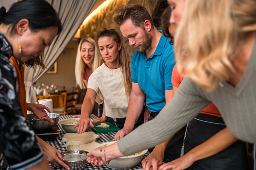 Multiracial group experience and learn the art of Chinese cuisine as they skillfully prepare ingredients for flavorful spring rolls delight on a cooking class with beautiful Chinese female chefs.