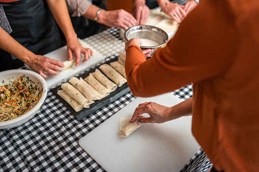 Close-up of multiracial group experience and learn the art of Chinese cuisine as they skillfully prepare ingredients for flavorful spring rolls delight on a cooking class with beautiful Chinese female chefs.