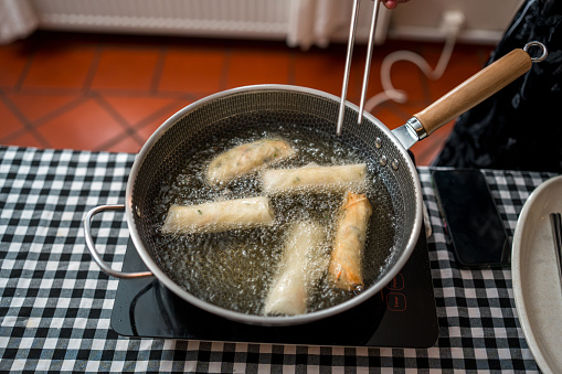 Chinese female chef is demonstrating how to pan-fry Chinese spring rolls in the kitchen on a cooking class.