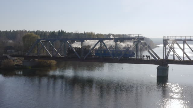Aerial view of an old steam locomotive traveling on a railway bridge over a river