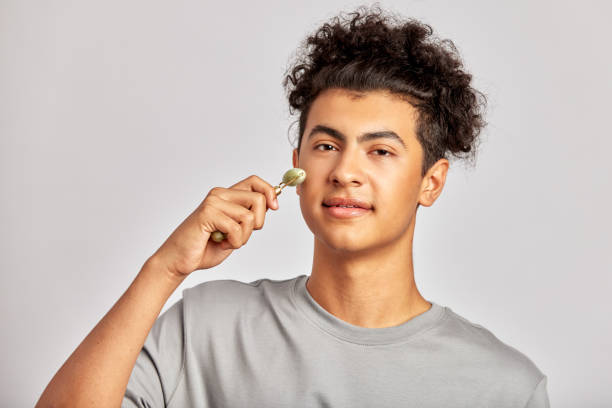 istock Young handsome smiling guy using jade de-puffing face roller to keep his skin soft and smooth. Swarthy man with black curly hair maintains his natural beauty with a skincare routine. Men's self-care. 1846914812