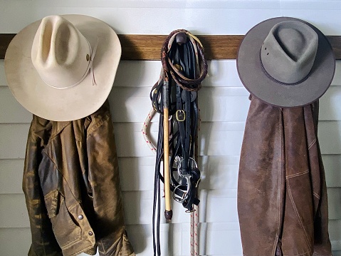 Horizontal still life of country stockhorse style cowboy riding jackets and hats with bridle on wood wall hook and bench on rural farm horse property Bangalow NSW Australia